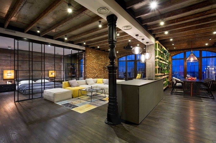aménagement de studio loft industriel aux murs briques et plafond avec poutres en bois, éclairage corde électrique avec ampoules