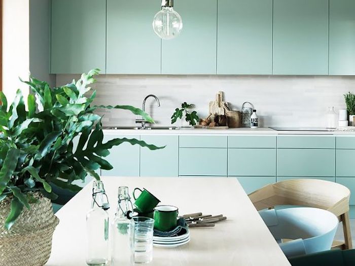 idee de facade cuisine bleu celadon, crédence grise, plan de travail en marbre, table blanc cassé, chaises beige, bleu et vert, feuilles de plantes vertes dans un panier