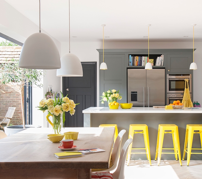 petite cuisine ouverte en gris avec bar gris et tabourets jaunes metalliques, ouverture sur salle à manger en table bois et chaises scandinaves