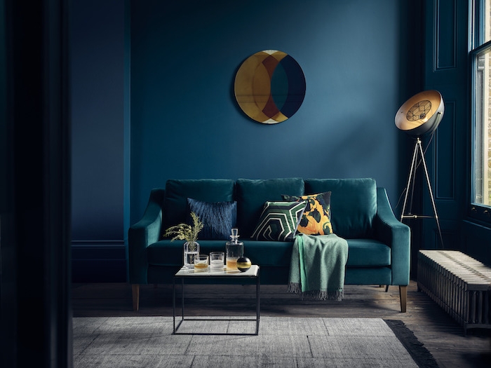 idée de salon bleu petrole avec canapé nuance bleu paon, couverture verte, table minimaliste noire avec plateau blanc, peinture murale bleu marine, tapis gris