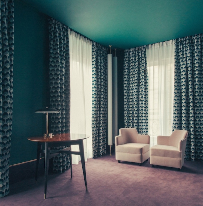 idee deco salon couleur bleu canard, nuance pétrole, fauteuils beiges, table en bois vintage, rideaux blanc, vert et bleu à motifs géométriques, tapis gris clair