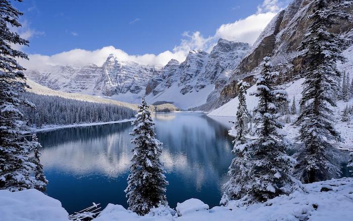 paysage hiver fond ecran, lac entouré de montagnes enneigées, arbres conifères et pins couverts de neige