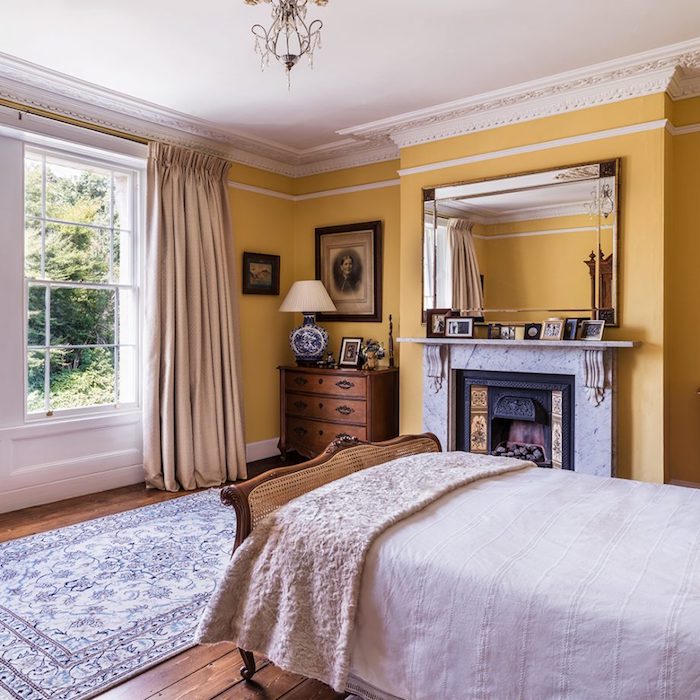 peinture chambre adulte jaune dans une pièce vintage, lit bois et commode vintage, linge de lit blanc, parquet marron, cheminée design