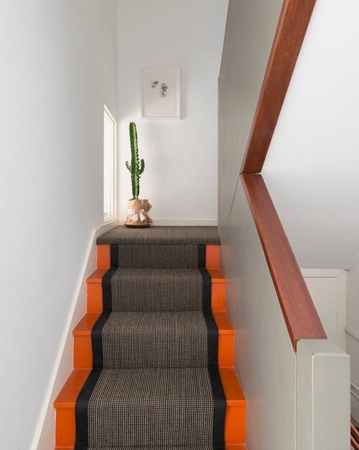 peinture escalier orange avec un tapis escalier gris et noir, une decoration verte de cactus dans un pot de fleur enveloppé de papier kraft