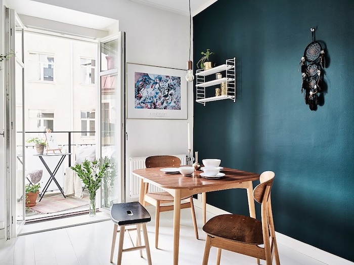 deco salle a manger avec un pan de mur pétrole, nuance de bleu foncée, table et chaises en bois, sol blanc, deco murale d attrape reve noir