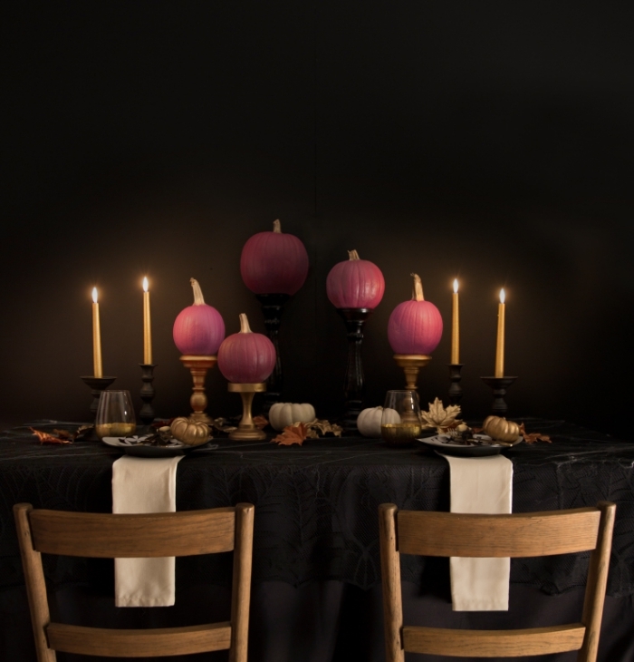 décoration de la table halloween avec nappe noire et bougeoirs en or, citrouilles peintes en rose sur table noir