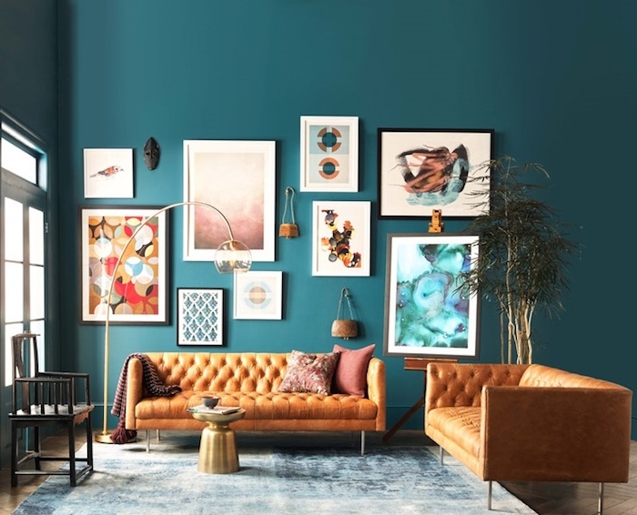 salon moderne bleu petrole peinture, deco murale de cadres colorés originaux, canapé en cuir orange, tapis bleu et blanc, table basse couleur or