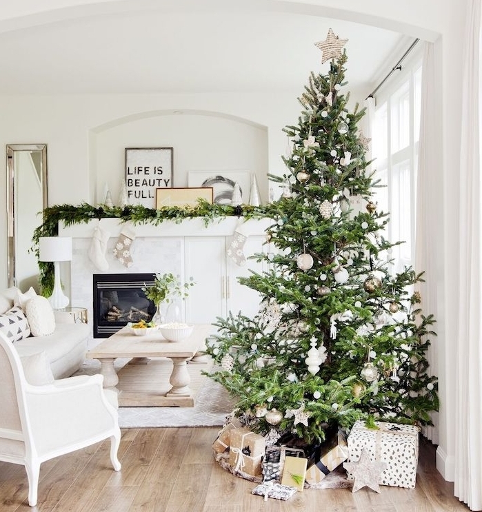 salon scandinave en blanc avec sapin de noel decoration en ornements blanches, canapé, chaise blancs, cheminée décoré d une guirlande de pin