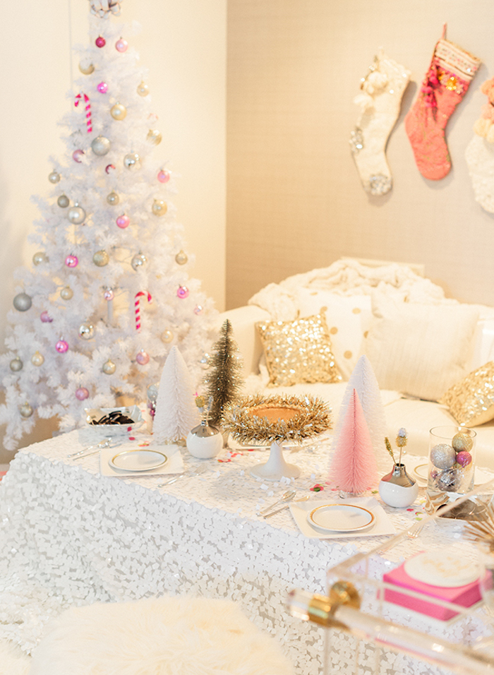 modele de sapin de noel blanc, décoré de boules de noel rose, or et argent, canapé et nappe table blanche, chaussettes suspendues au mur et détails déco dorés