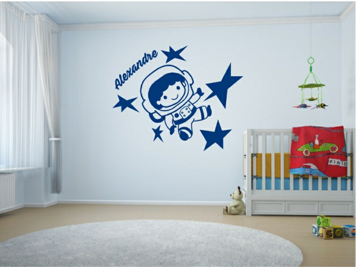 stickers chambre bébé avec le nom de l'enfant et petit cosmonaute qui explore le cosmos au mur au dessus du lit blanc