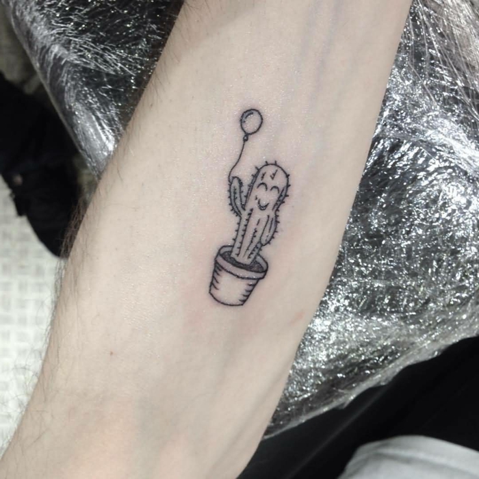 tatouage discret, petit cactus noir en pot au visage aimable et tenant un ballon