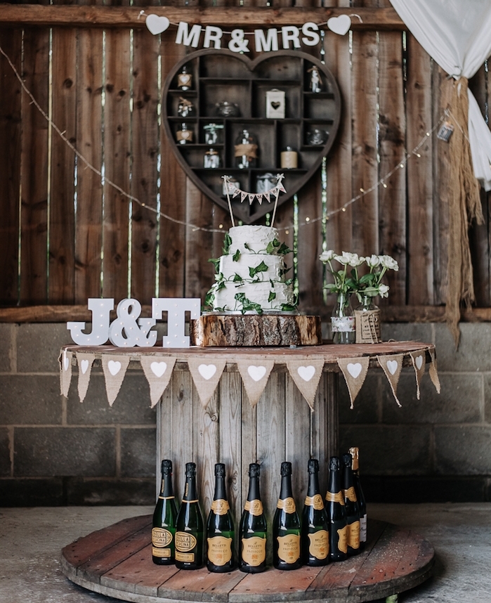 touret bois deco, idée de table gateau de marage, champetre chic, gâteau blanc sur un rondin en bois, lettres capitales mariés, fleurs dans des bouteilles en verre, bouteilles de champagne