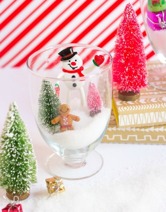 un verre simple décoré avec des figurines de sapin de noel, bonhomme de neige sur de la neige artificielle, boule a neige, activité manuelle primaire