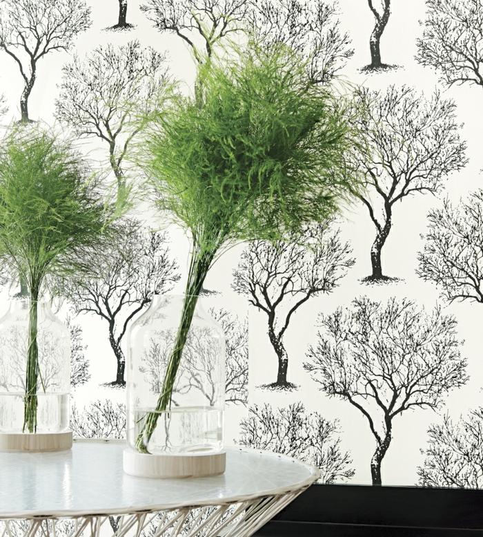 poster geant avec des arbres en noir sur fond blanc, mur d'entrée, table d'entrée en métal blanc, deux vases avec des plantes vertes en forme d'arbres, papier peint trompe l'oeil