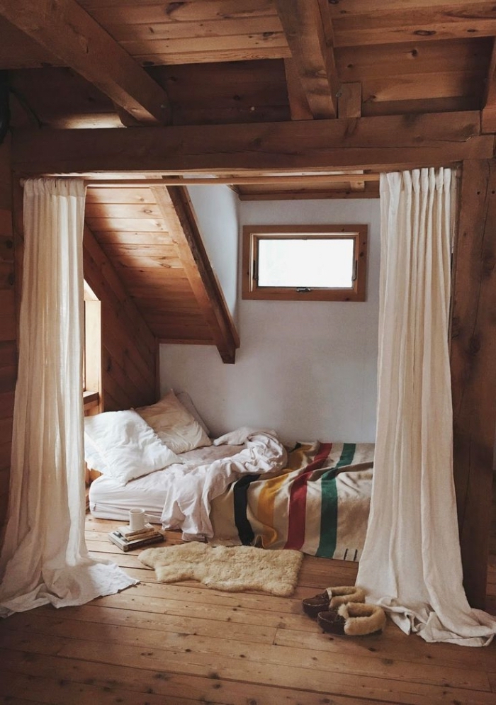 chambre mansardée, petite pièce aux murs blancs avec plafond en poutres bois foncé et petite fenêtre de bois 
