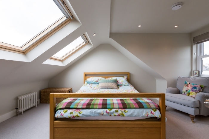 chambre a coucher, cadre et tête de lit en bois marron clair, éclairage led sur plafond blanc, couverture de lit et coussin multicolore