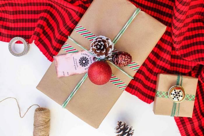 paquet cadeau noel, une boite enballée de papier kraft avec decoration de bandes de washi tape rouge, blanc et vert, pomme de pin, ornement et étiquette noel