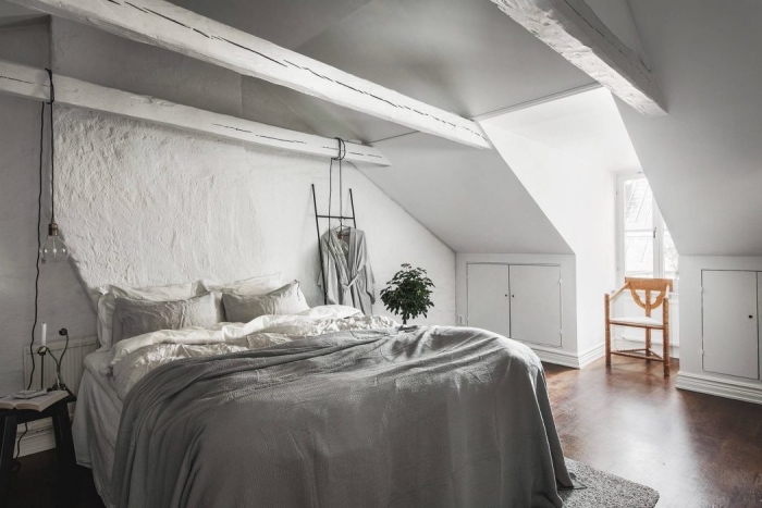 comble aménagé, chambre blanche avec poutres en bois peint blanc et plancher marron, grand lit avec couverture grise