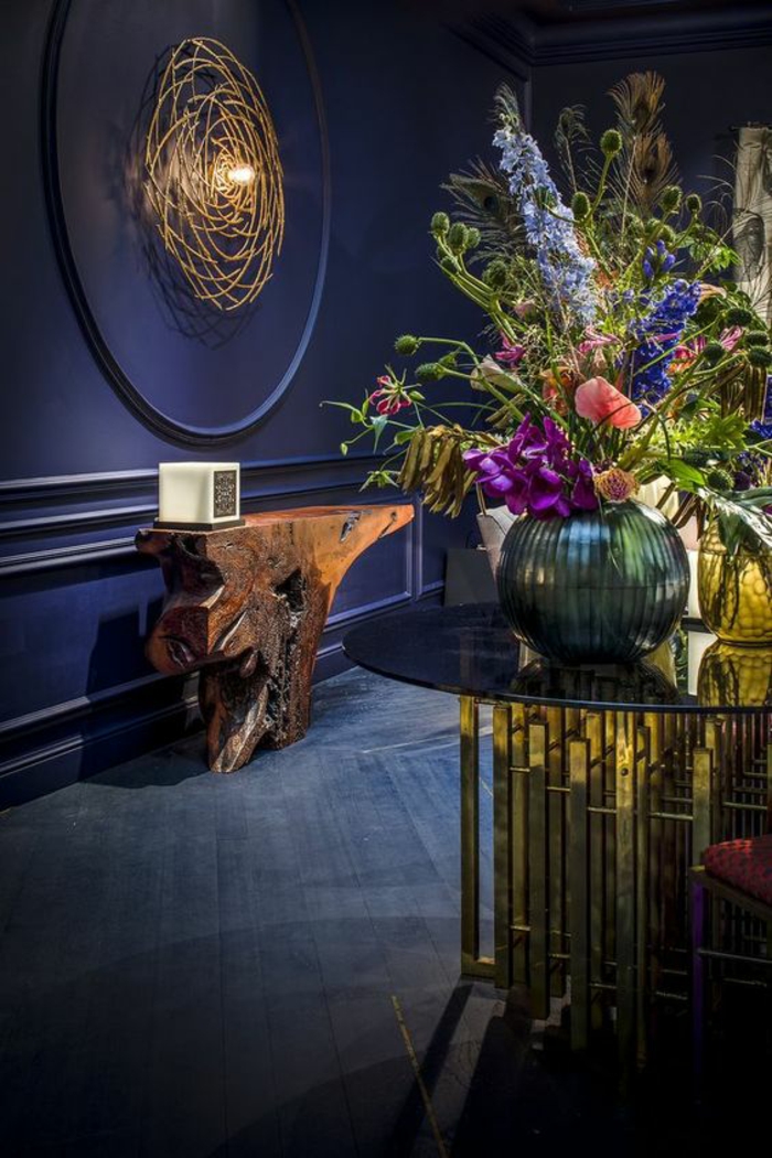 deco couloir en bleu électrique avec frise taille grande et en forme ronde illuminée par une ampoule, table design en forme de tronc d'arbre stylisé, grande table ronde en verre trempé et en parties métalliques dorées