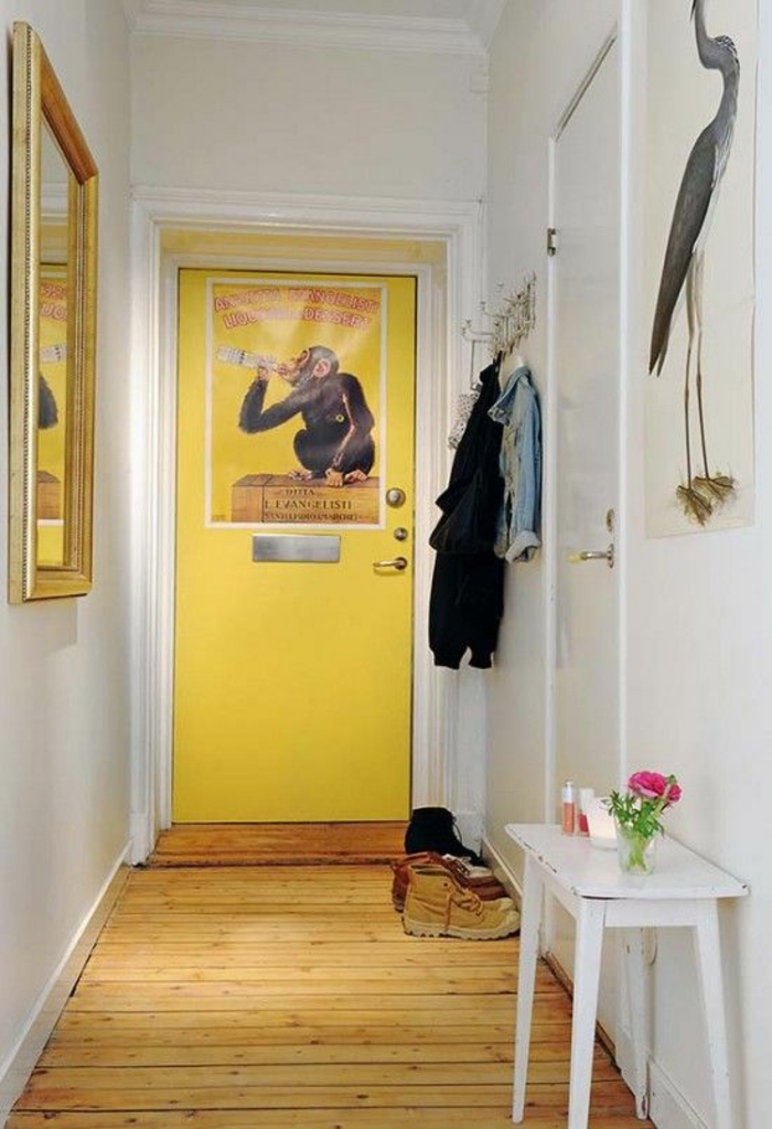 deco couloir, murs blancs, porte jaune, parquet en bois brut jaune, table rectangulaire peinte en blanc, grand miroir carré avec cadre doré posé en face d'une porte blanche 