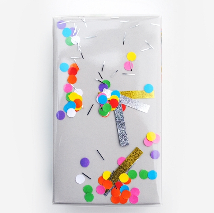 emballer cadeau, idée simple de paquet en papier gris et plastique avec des confettis colorés et bandes pailletées dessous