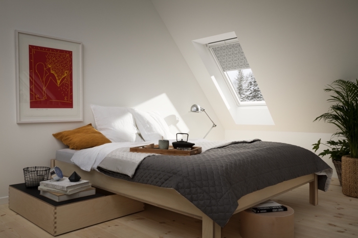 chambre mansardée aux murs blancs avec petite fenêtres de plafond et plancher en bois stratifié clair