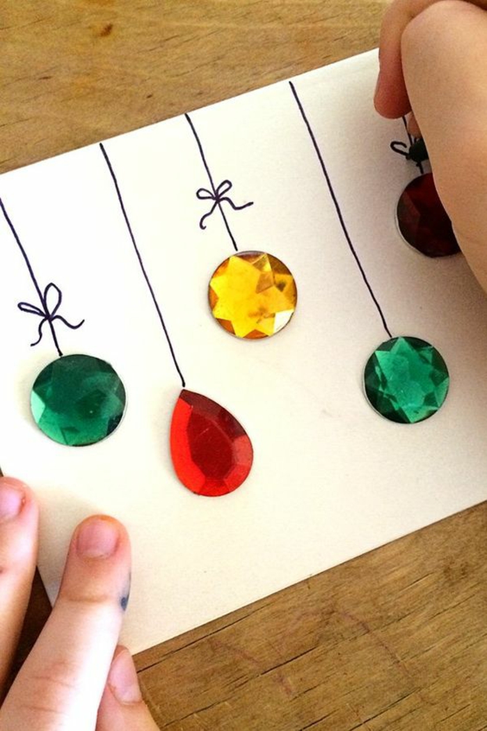 activite manuelle noel sur du carton blanc, avec des éléments décoratifs autocollants en vert, jaune et rouge, qui imitent les boules sur le sapin