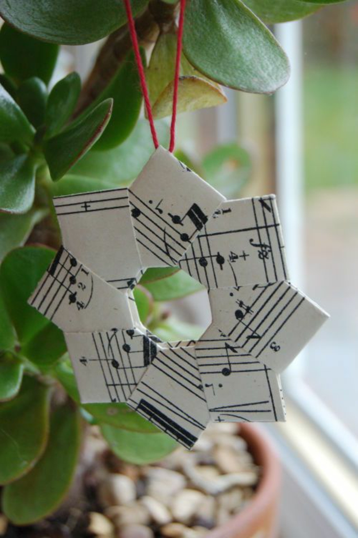 bricolage de noel avec étoile créée avec des parties de partitions musicales et du fil rouge pour suspendre sur une plante dans la maison ou sur un arbre de noël 