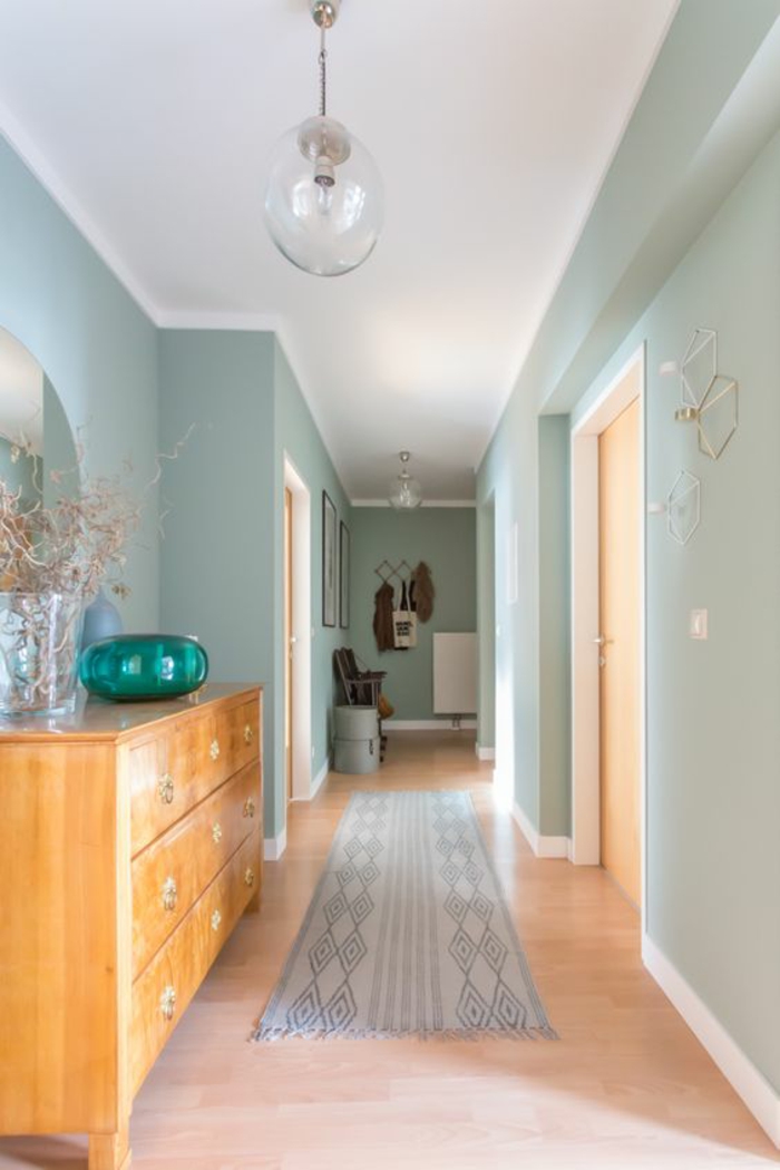 deco couloir en bleu pastel et blanc, avec tapis en gris clair et blanc, lampadaire en forme de boule en verre transparent, murs en bleu pastel, grand meuble en bois clair avec bol décoratif en verre vert émeraude