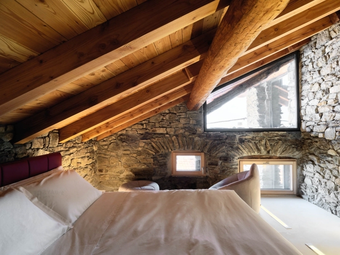 chambre à coucher de style rustique et campagne avec revêtement des murs en pierre et plafond avec poutres en bois