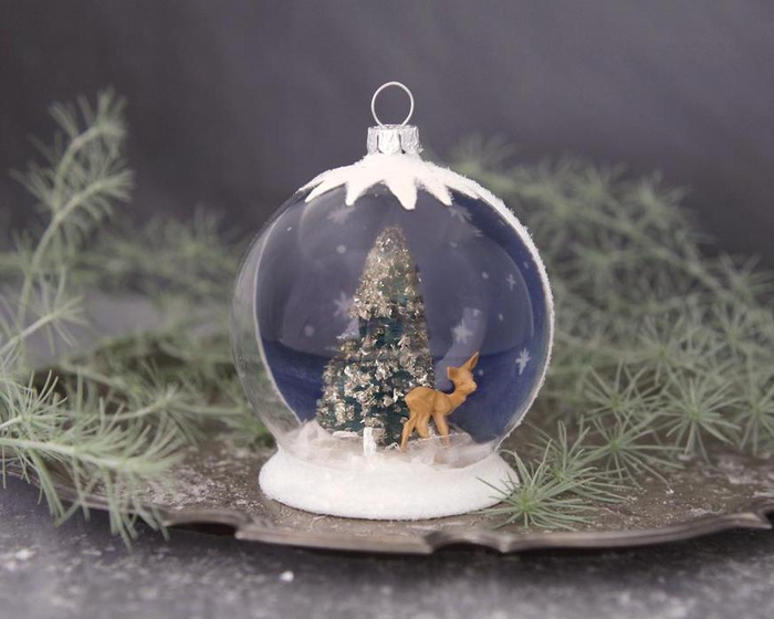 une decoration de noel fait main qui représente une boule de neige semi-transparente à peinture effet neige, avec des figurines de noël à l intérieur du globe