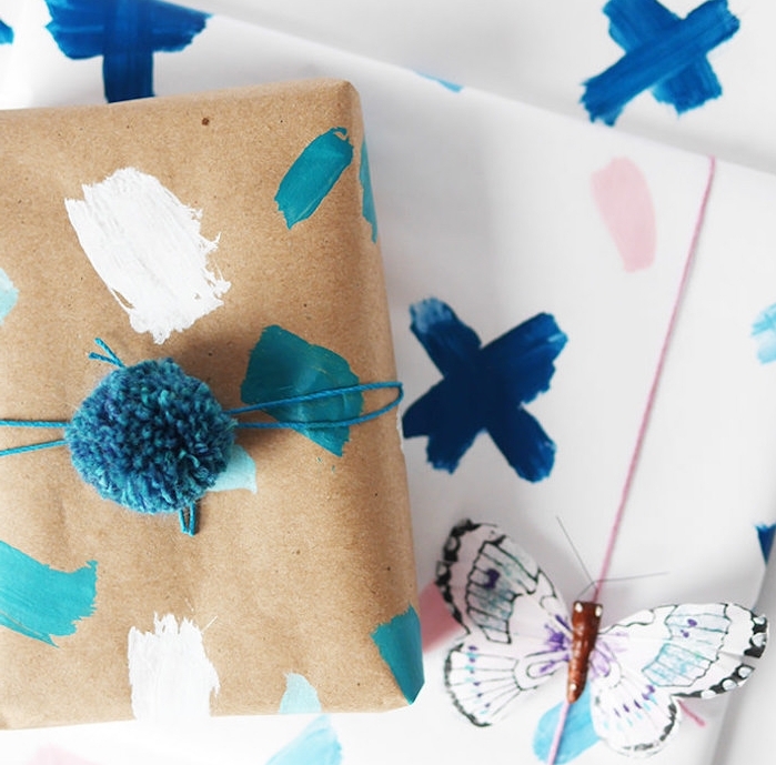 modele emballage cadeau original, papier blanc et papier kraft avec des touches de peinture, pompon bleu et papillon décoratif