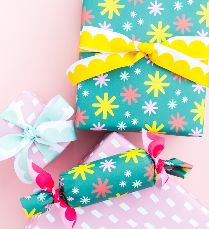 papier cadeau noel couleur bleue et motifs flacons de neige colorés, paquet en forme de cube et cylindre et ruban bleu, rose et jaune