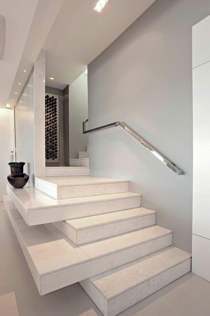 escalier design avec des marches en blanc disposées en manière irrégulière, certaines dépassant les autres, avec poignée fixée sur le mur en couleur argent luisant, grand vase décoratif en noir sur l'une des marches 