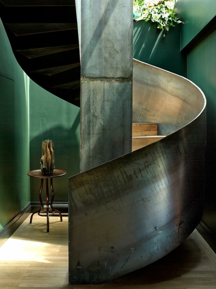 escalier moderne métal, murs de la pièce en vert, escalier en colimaçon, petite table ronde basse en fer forgé, avec vase arty en pierre, sol avec revetement en bois PVC clair 