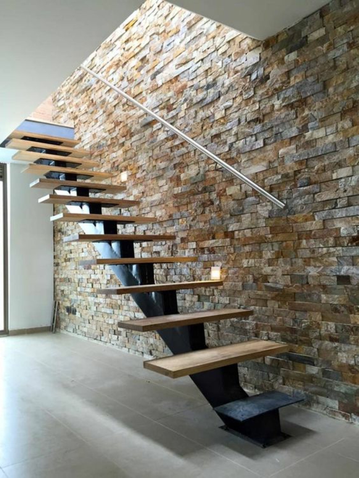 escalier moderne, escalier design, avec des marches en bois clair sur base métallique noire, murs en pierres multicolores, en couleurs claires, simple poignée minimaliste en couleur argent