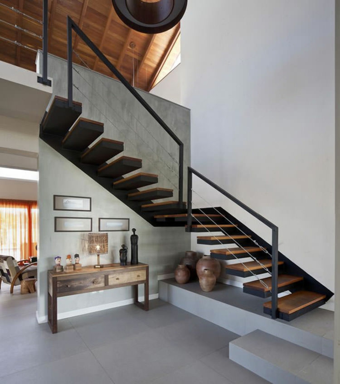 escalier design en métal noir et bois en couleur marron, dans un intérieur en style industriel, avec plafond haut, quatre vases décoratives en céramique beige, trois tableaux en forme rectangulaire 