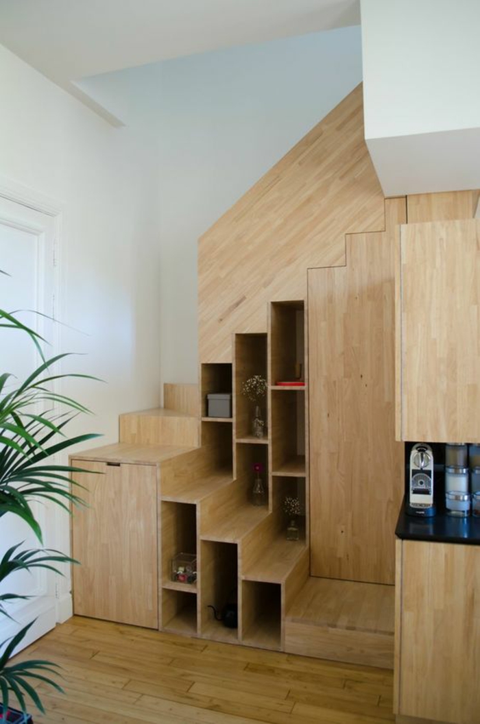 escalier design en bois PVC clair avec bibliothèque à plusieurs niveaux insérée, sol recouvert de parquet en bois clair, grande plante verte palmier dans un pot, plafond blanc,