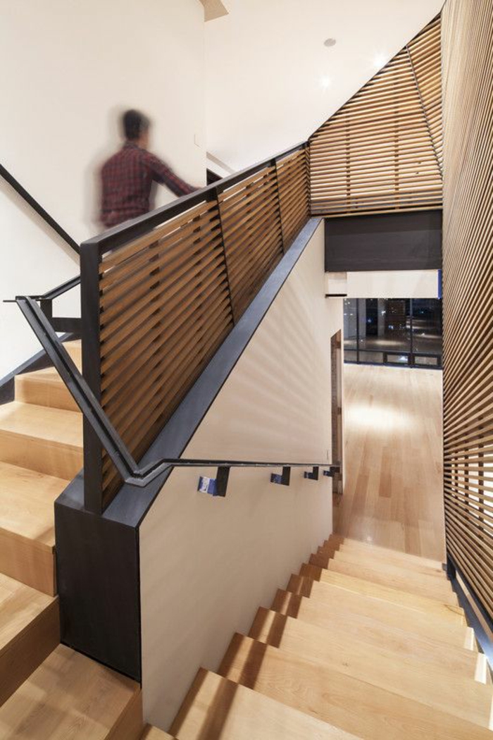 escalier design en bois clair, avec garde corps en métal noir, murs en beige, garde corps avec des bandes fines de bois clair 