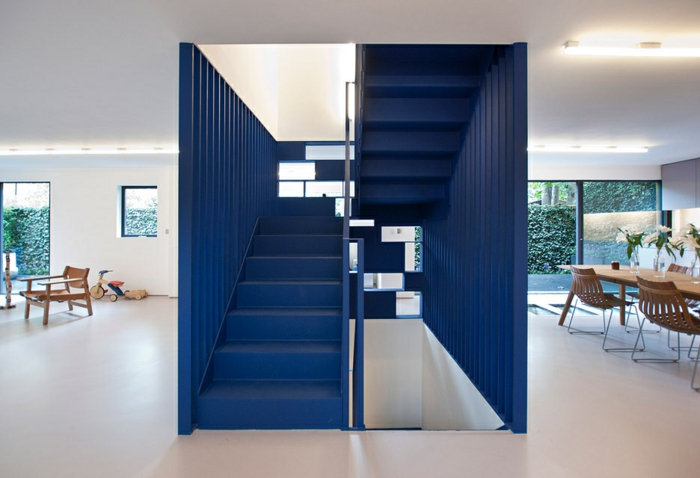 escalier design en bleu marin avec revetement en métal en forme de cube, sol avec carrelage beige luisant, table et chaises en bois clair