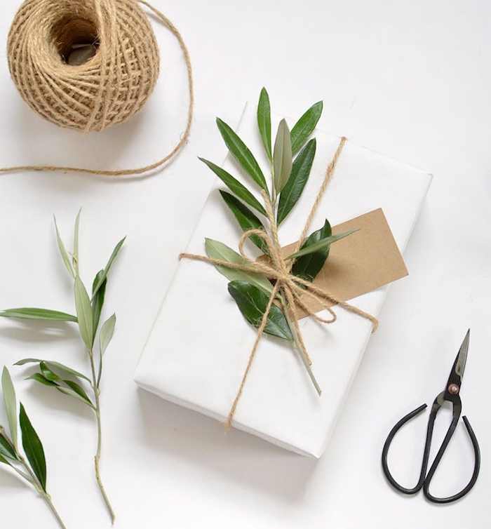 boite cadeau noel enveloppée de papier blanc, branches vertes et étiquette en papier kraft comme décoration