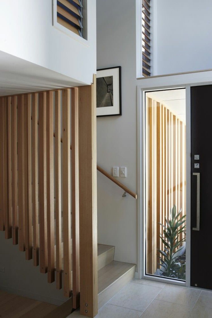 escalier moderne, escalier design en bois clair, avec des motifs rayures en bois comme garde corps, sol en dalles en couleur ivoire, marches en couleur ivoire, tableau avec cadre noir, poignée d'escalier minimaliste en bois clair 