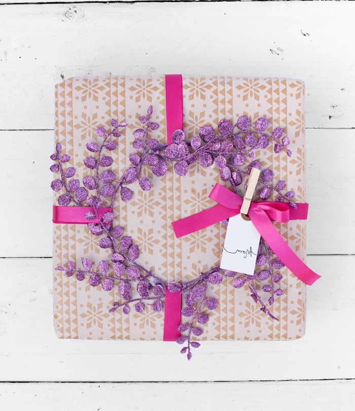 papier cadeau noel gris à motif frise de flacons de neige, ruban mauve et couronne de branches violettes pailletées