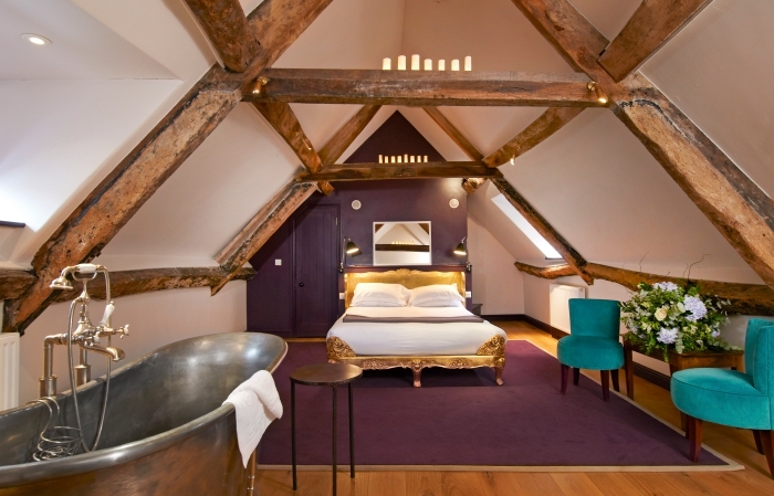 aménagement moderne du grenier avec fauteuil turquoise tapis violet et cadre de lit doré, baignoire dans la chambre à coucher sous combles