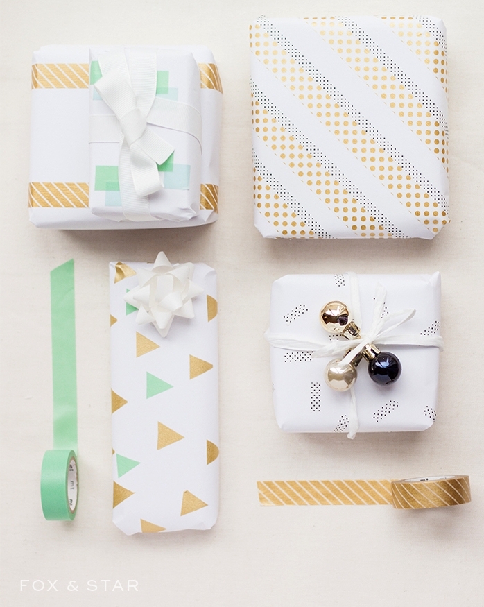 boite cadeau noel enveloppée dans papier blanc avec décoration en triangles et bandes de washi tape, ruban et petites boules de noel