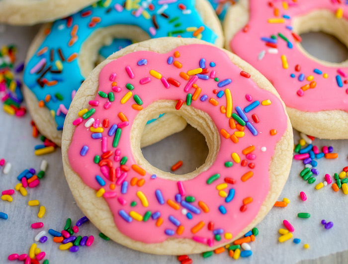 biscuits en forme de beignet, donut décoré de glacage sucre blanc coloré en rose et vermicelles de sucre colorés