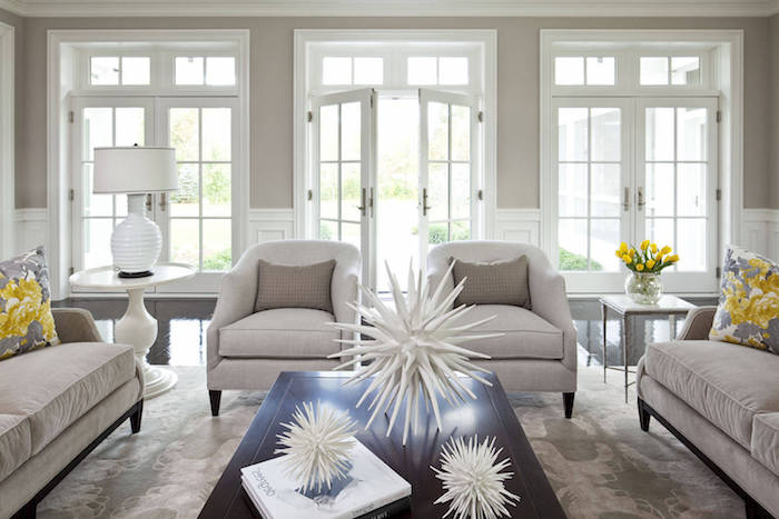 canapés, fauteuils et mur gris clair, nuance taupe dans un salon en gris et blanc avec des accents jaunes, table basse bois marron