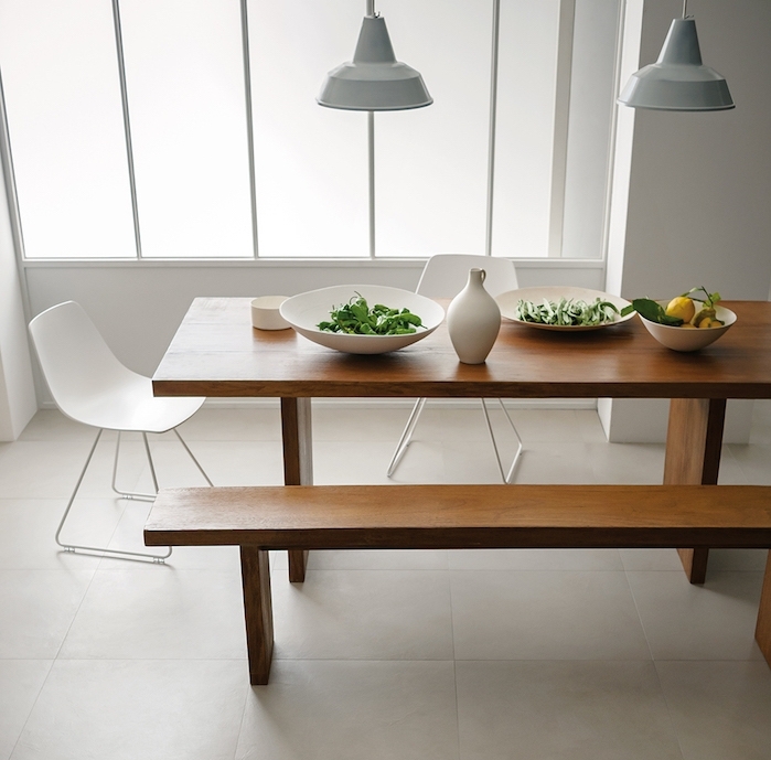 salle à manger carrelage sol couleur grege, table et banc en bois massif, chaises scandinaves blanches, suspensions gris clair, murs blancs