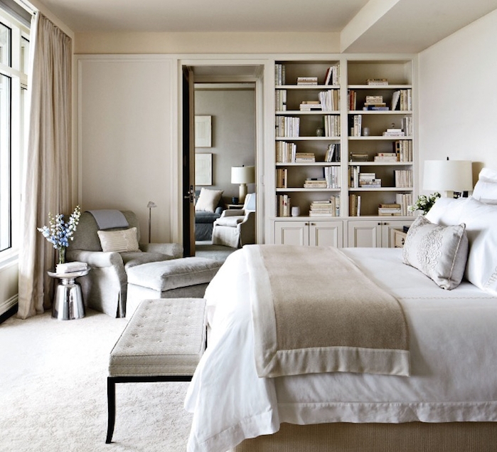 exemple d amenagement chambre à coucher couleur taupe clair, linge de lit gris et blanc, fauteuil et tabouret gris, bibliothèque encastrée dans un mur