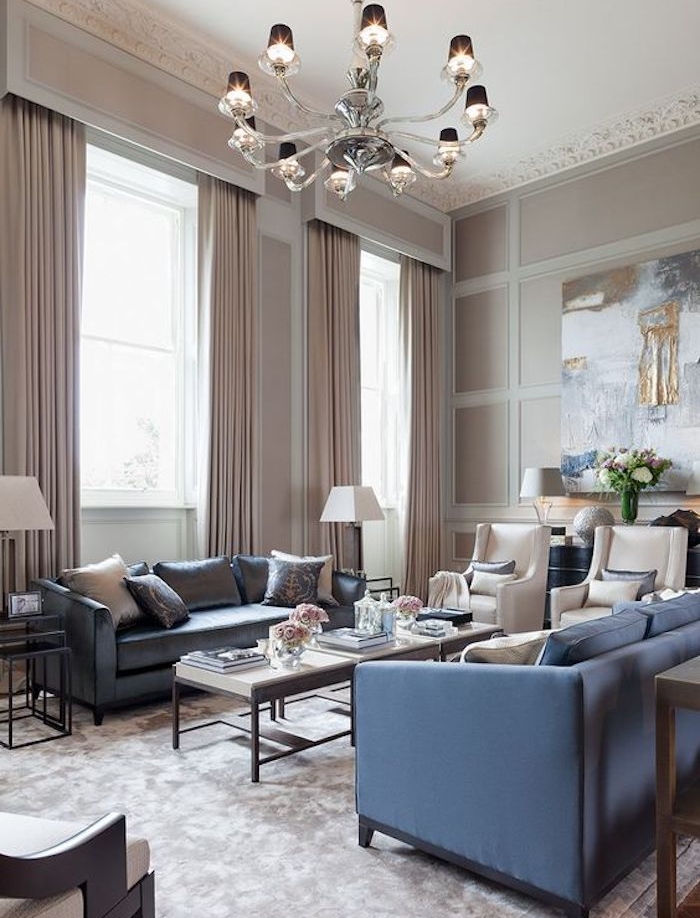 murs et rideaux couleur gris taupe, canapés bleus, tapis gris, fauteuils grege, tables basses en bois, lustre exubérant